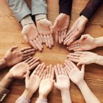 Top view of diverse hands forming a circle on a wooden table, symbolizing unity and diversity.