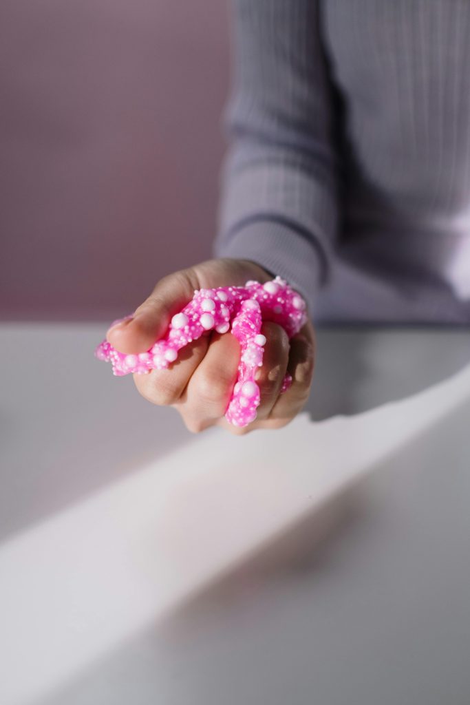 A hand holds vibrant pink foam slime, showcasing texture in soft lighting.